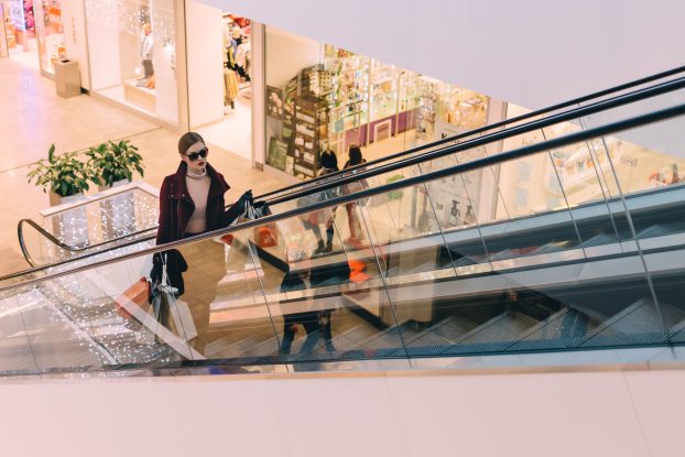 Woman riding an escalator in a shopping mall holding bags